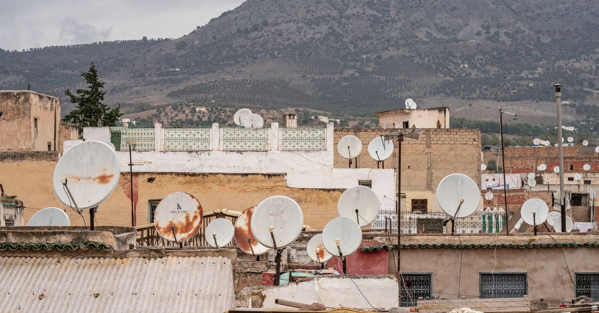 Rustic rooftops with satellite dishes in Fes, set against a rolling hill landscape.